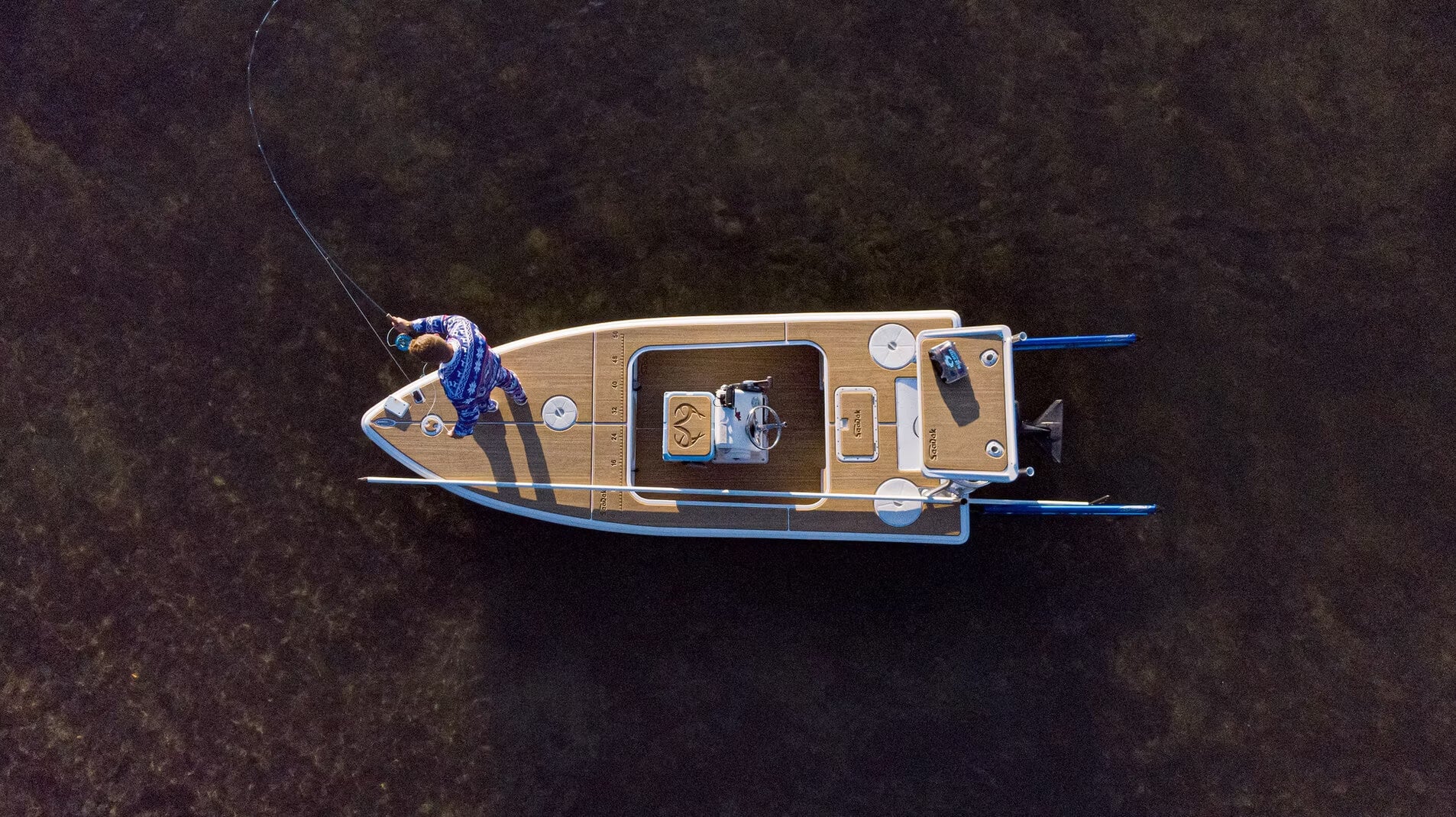 Man casting a fishing line on a skiff with a custom SeaDek kit featuring woodgrain laser patterning and a Realtree logo on his custom SeaDek cooler top. 
